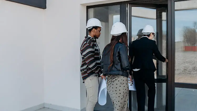 Equipo técnico con cascos de seguridad y planos ingresando a un edificio para coordinar un servicio de limpieza de fin de obra con Klinn.