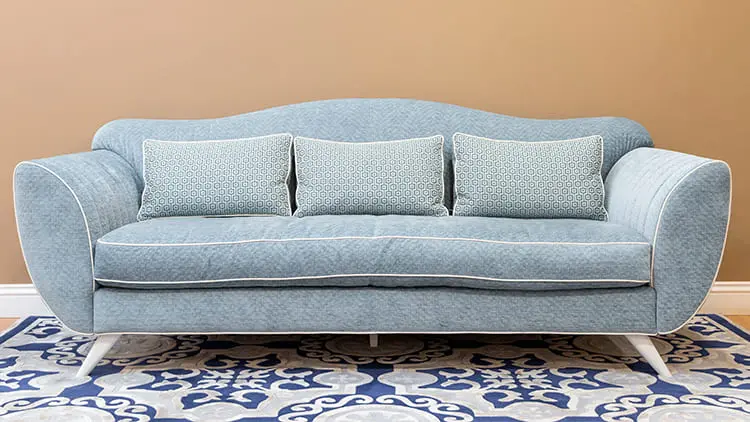 Sofá de tela azul moderno y alfombra estampada, ambos impecables y desinfectados tras un servicio de limpieza profesional de Klinn.