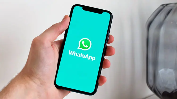 Mano sosteniendo un teléfono móvil con el logo de WhatsApp en pantalla para solicitar presupuesto de limpieza con Klinn.