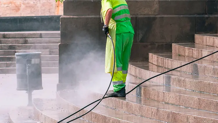 Operario con uniforme reflectante realizando el lavado a presión de escaleras y fachadas de piedra con el servicio exterior de Klinn.