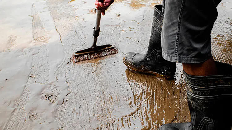 Operario con botas industriales lavando y eliminando lodo acumulado durante la limpieza de un tanque de agua subterráneo con Klinn.