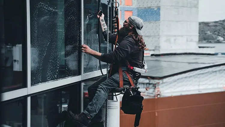 Técnico especializado con arnés de seguridad realizando la limpieza de cristales en altura de un edificio comercial con Klinn.